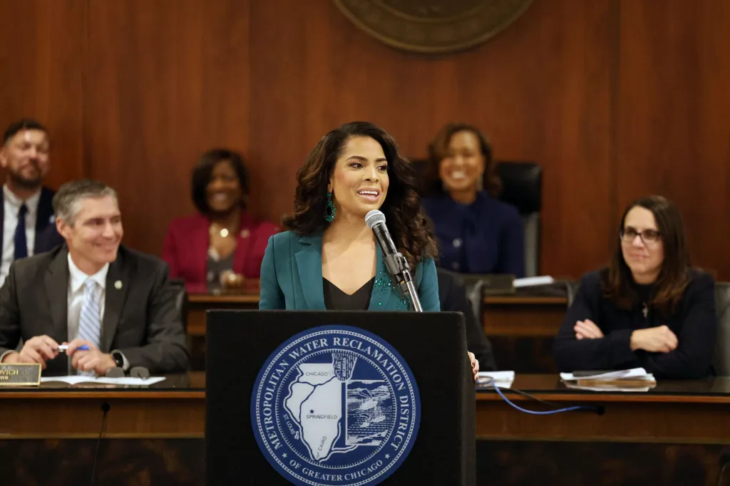 Precious Brady-Davis se tient sur un podium avec le sceau du Metropolitan Water Reclamation District of Greater Chicago, s'exprimant dans un microphone lors d'une réunion publique.